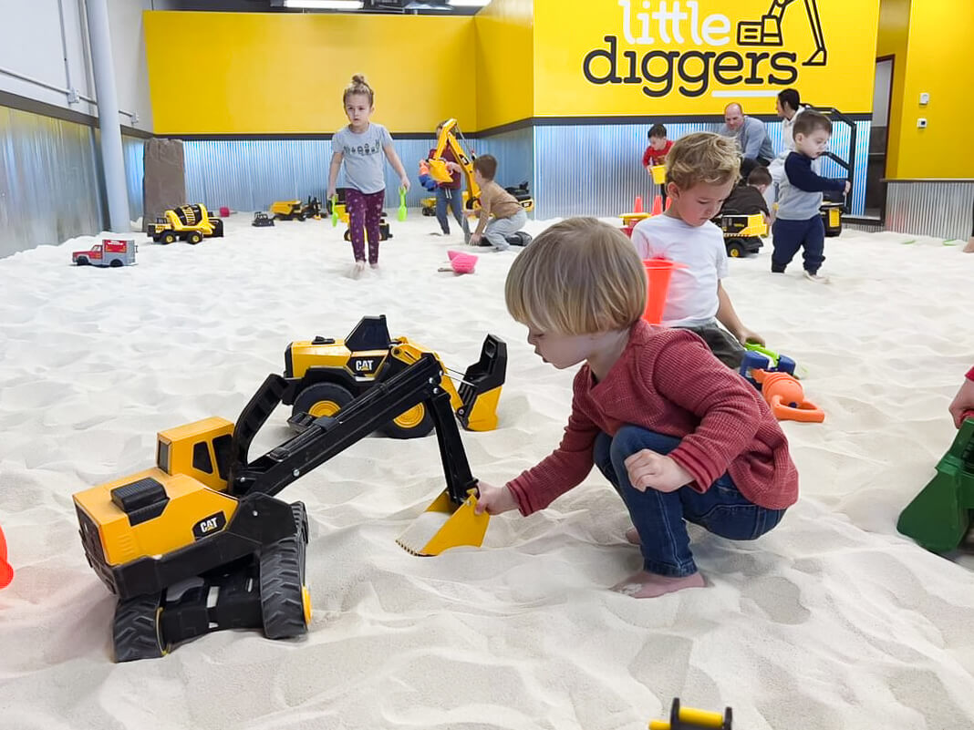 Child engaging sensory skills while playing with an excavator in the sand. The little one explores textures, feeling the grains of sand and manipulating the excavator, fostering sensory and fine motor development through play.