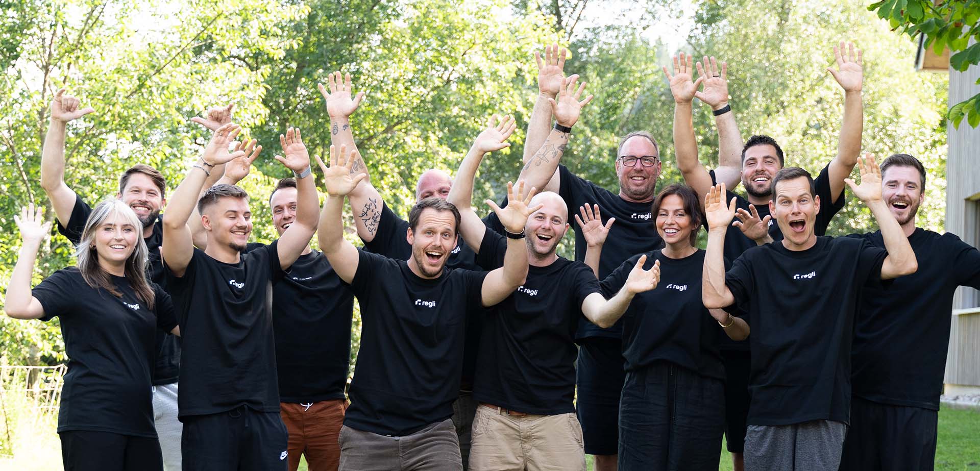 Regli Mitarbeiter Gruppenfoto mit schwarzen Regli T-Shirts vor grünen Bäumen 