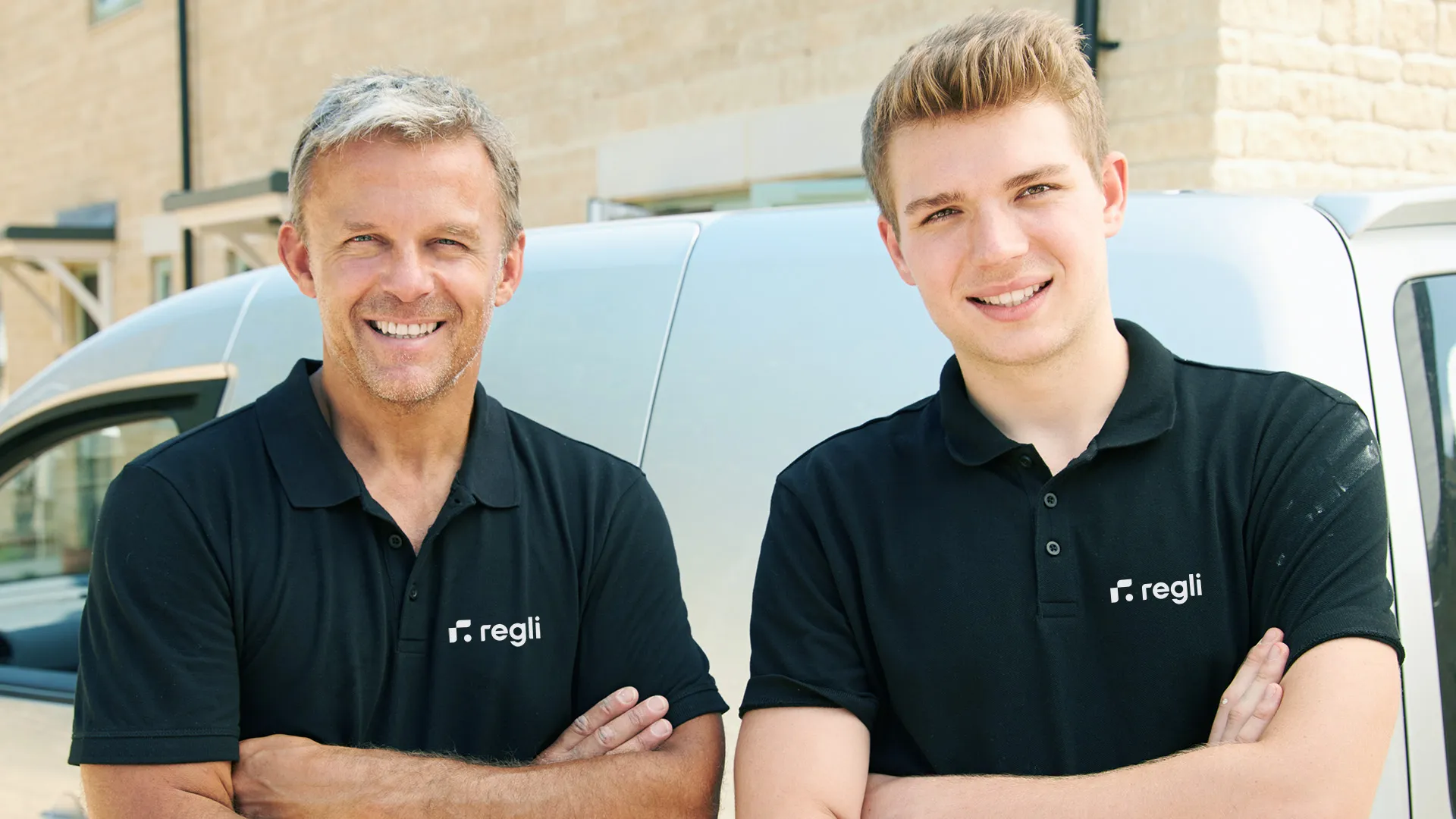 Regli employee two white men in black Regli t-shirt in front of white Tesla electric car in background 