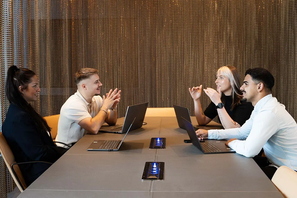Regli Mitarbeiter zwei Maenner zwei Frauen sitzen an Schreibtisch hinter vier laptops gegenueber diskutieren 