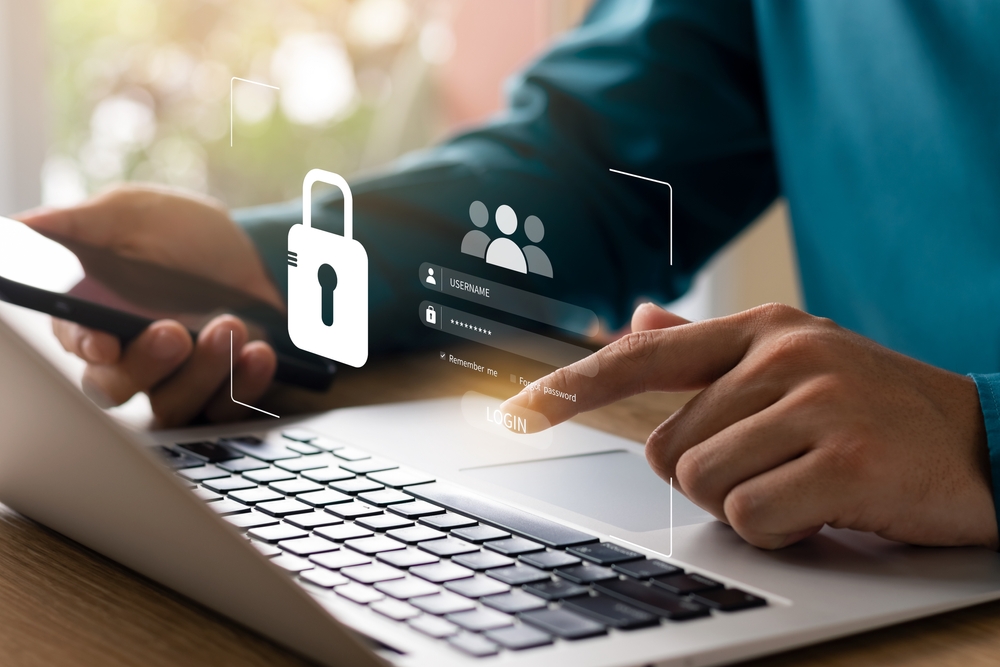 Person verwendet Smartphone und Laptop für sicheres Login mit sichtbarer digitaler Datenschutz-Symbolik