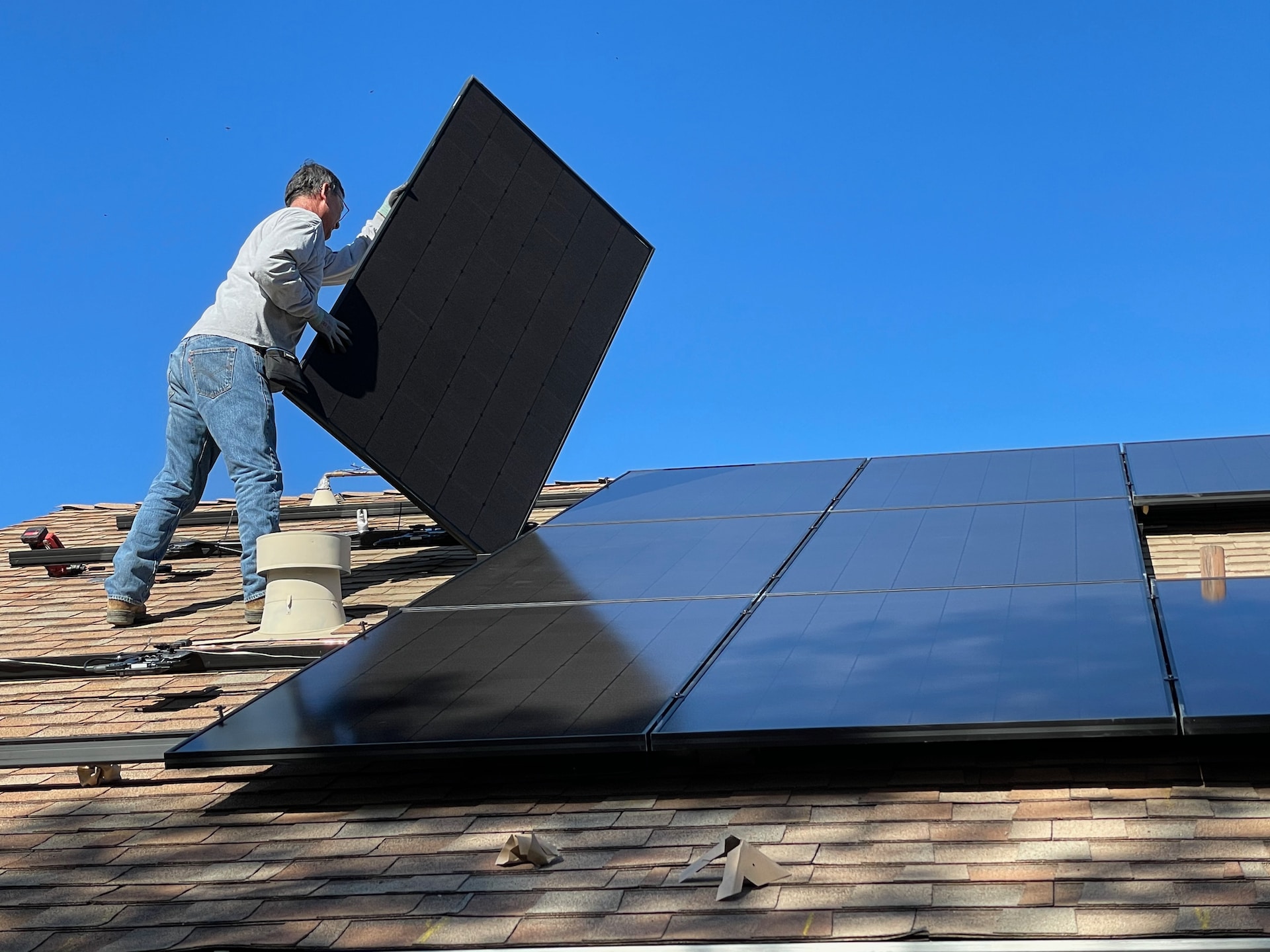 Auf Hausdach steht Mann der Solarpanels installiert, blauer Himmel Sonne scheint