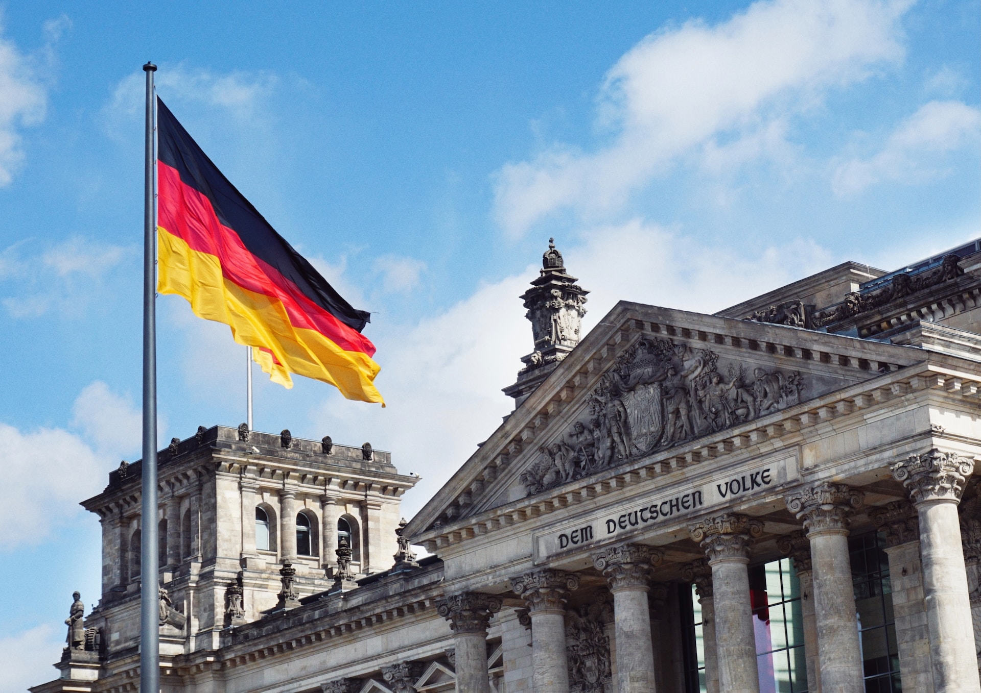 schräge Vorderansicht Deutscher Bundestag Detschland Fahne weht vor Bundestag, blauber Himmel, weiße Wolken Sonne scheint