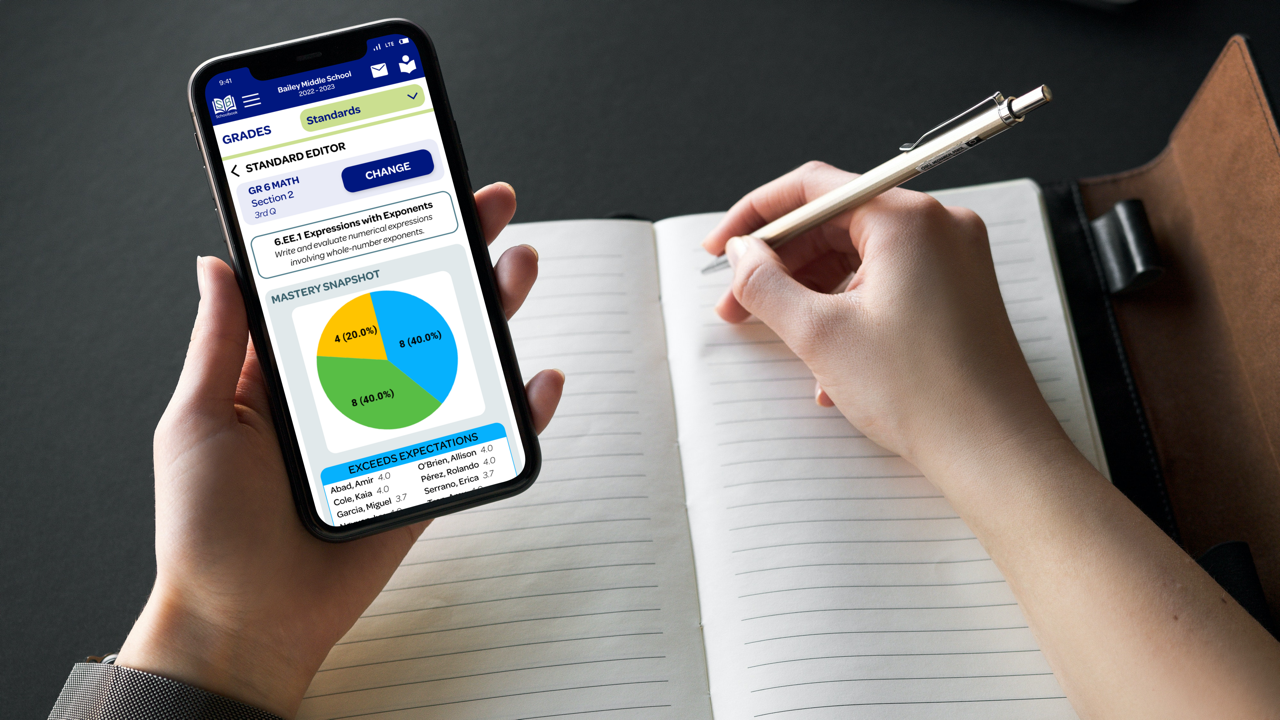 Person holding a phone in one hand while holding a pencil and writing in a notebook with the other; the phone screen shows the Standards page