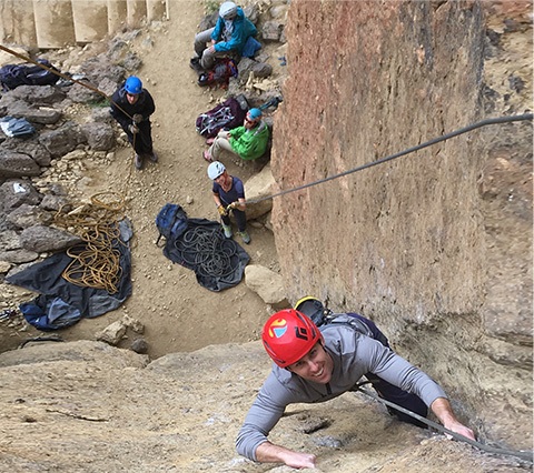 A climber using a wedge to grip the rock while looking up and smiling 