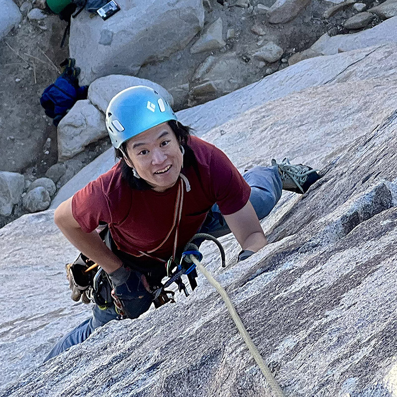 A man climbing up a mountain with a helmet on.