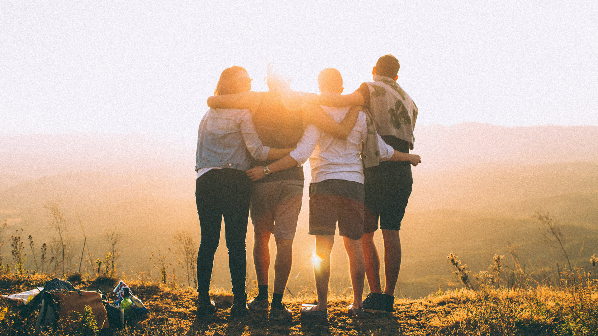 Group of friends embracing and admiring a landscape view, backlit by the sun.
