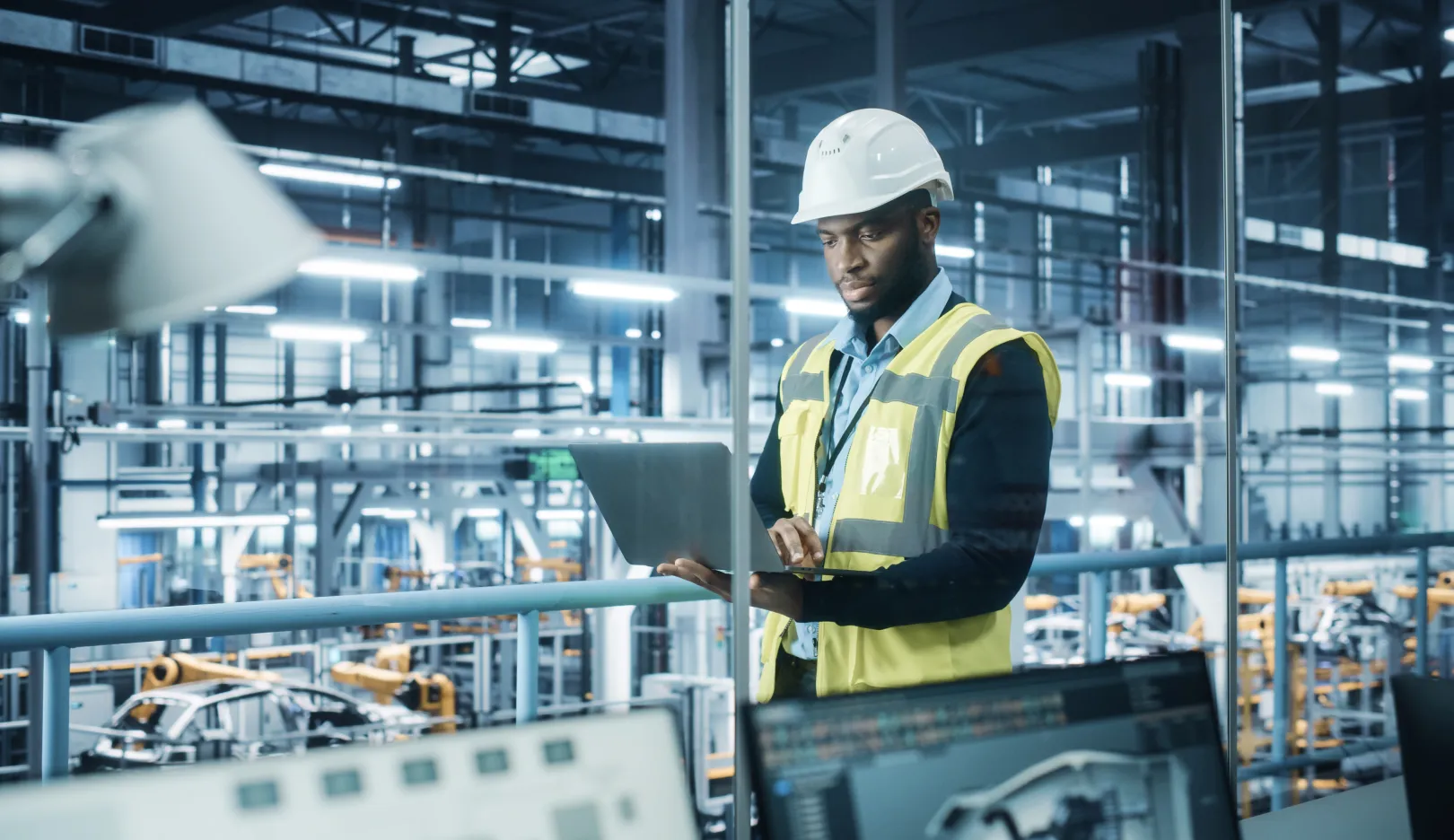 Man standing in a vehicle assembly factory and working on a laptop