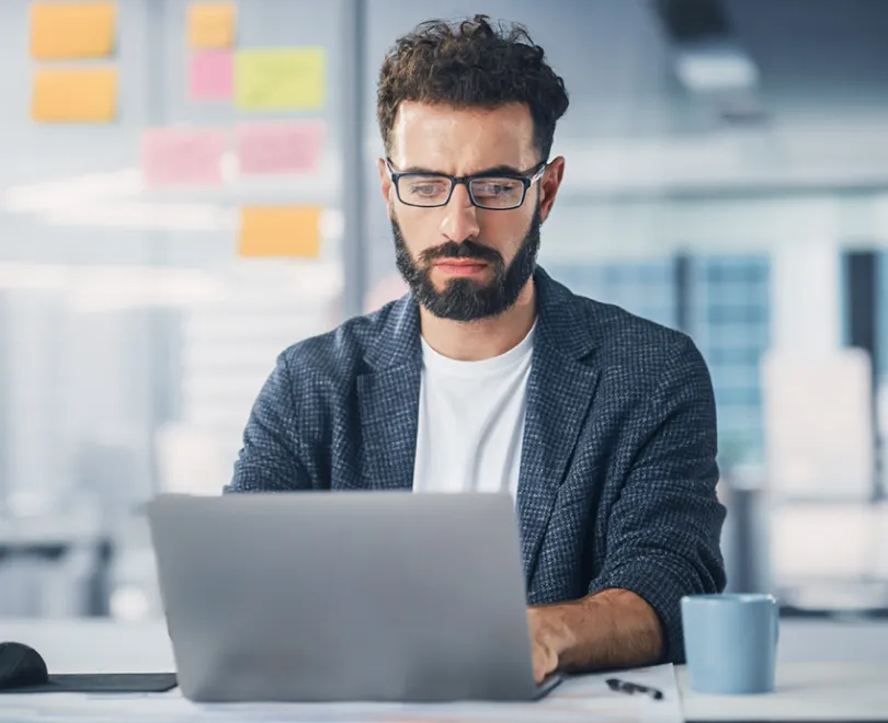a man with a beard and glasses using a laptop