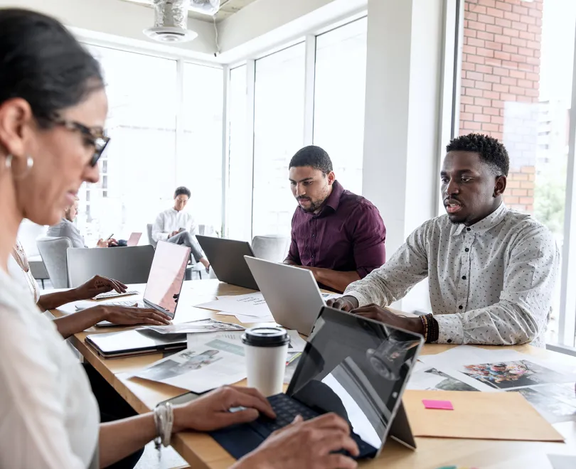 a group of people sitting at a table working on laptops