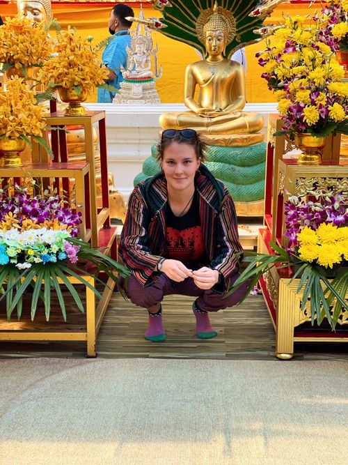 A woman sitting across a Buddha surrounded by flowers