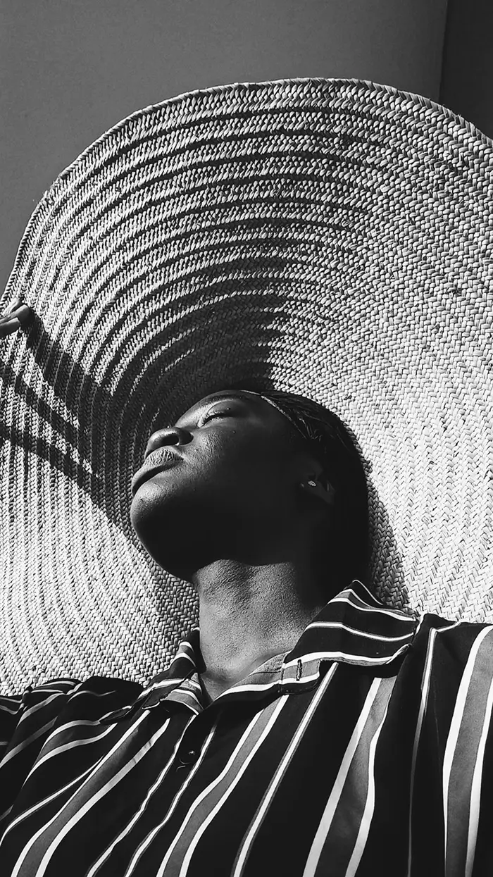 Woman wearing a large sun hat with eyes closed looking up at the sun edited with a black and white VSCO filter