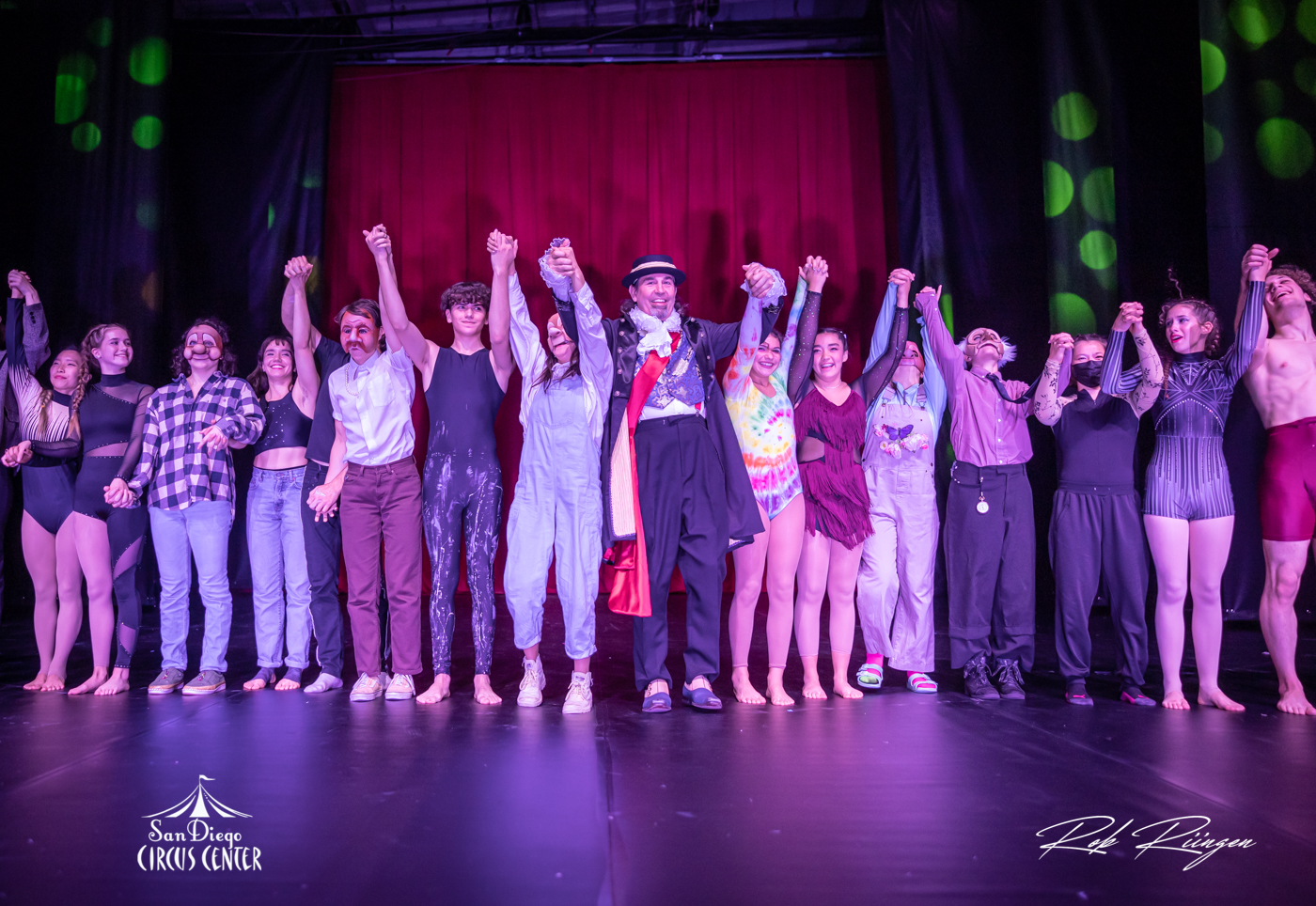 A group of circus artists holding hands for a bow at the end of a performance