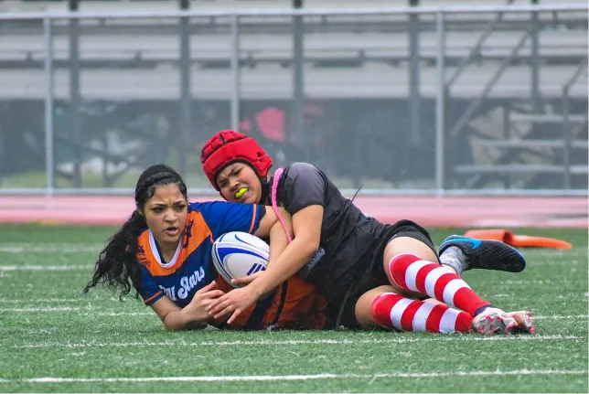 Two young women laying on the ground after a rugby tackle.
