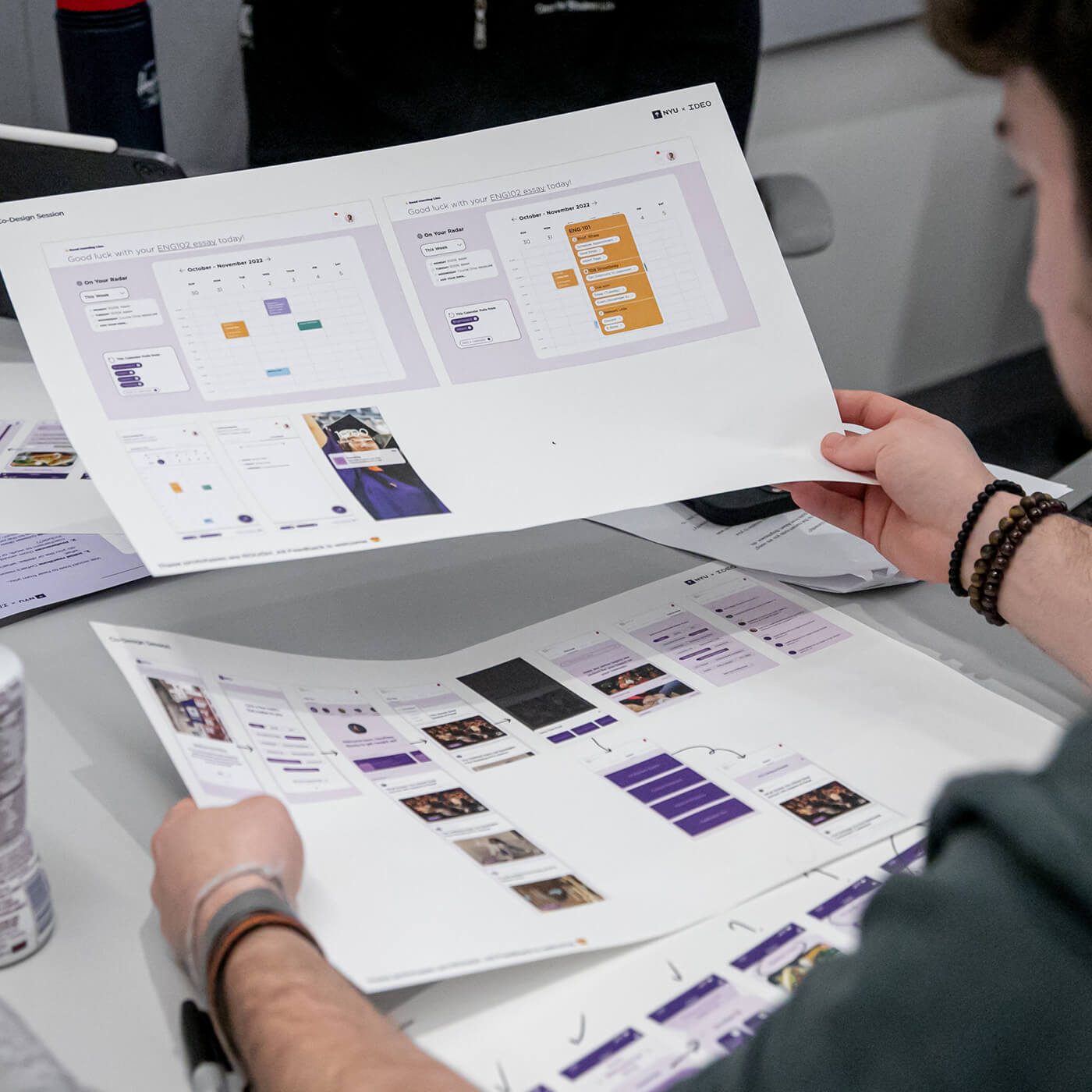 A new NYU student holds up large pieces of paper with prototypes of the new app on them.