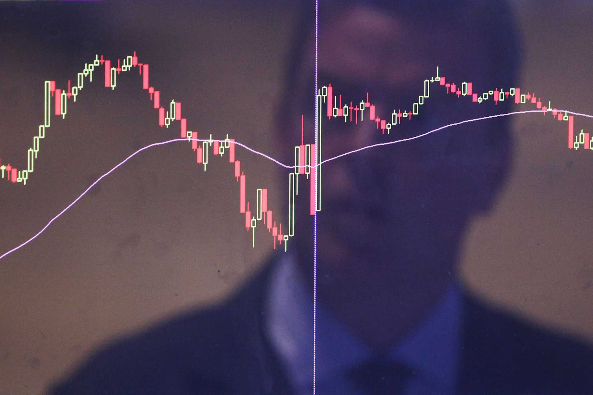 A man's face reflected in a stock market screen