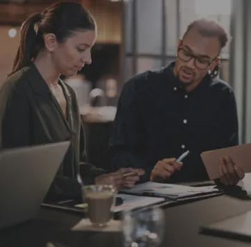 Two individuals collaborating on a laptop in a professional workspace.
