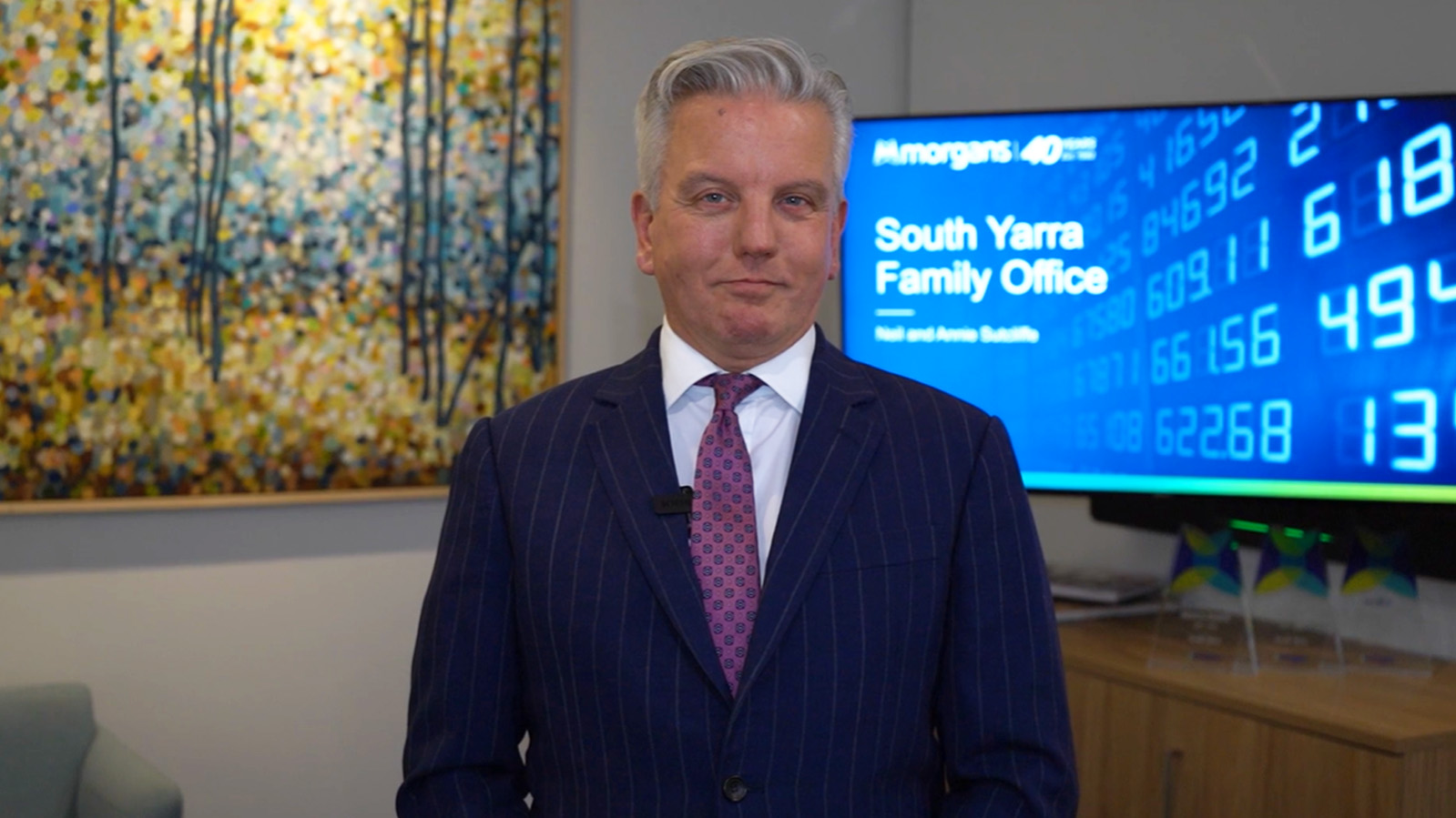 A man in a suit standing in front of a television.