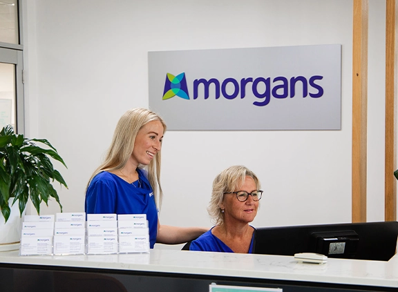 Two women sitting at a desk in front of a morgans sign.