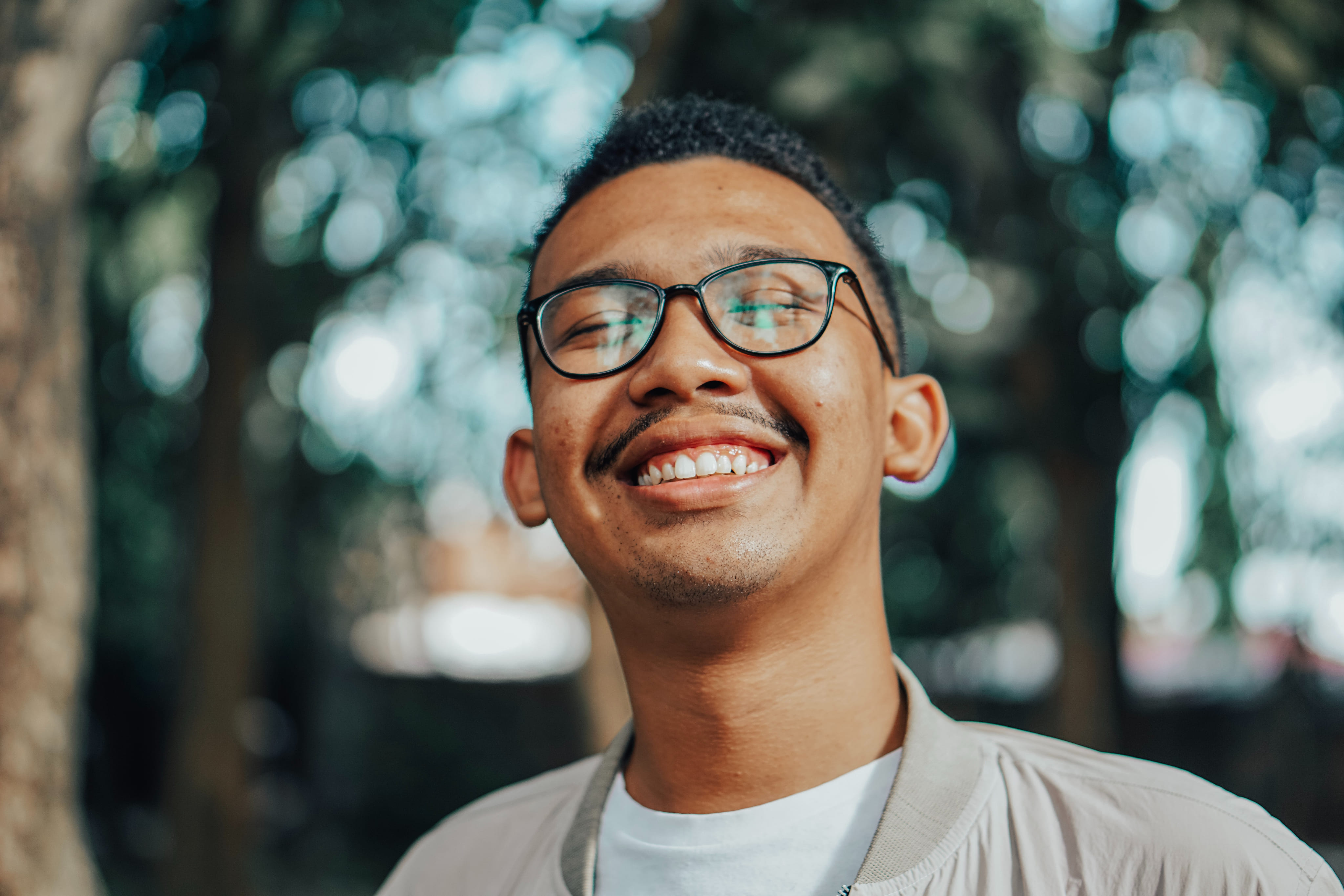 a man with glasses smiling in front of trees