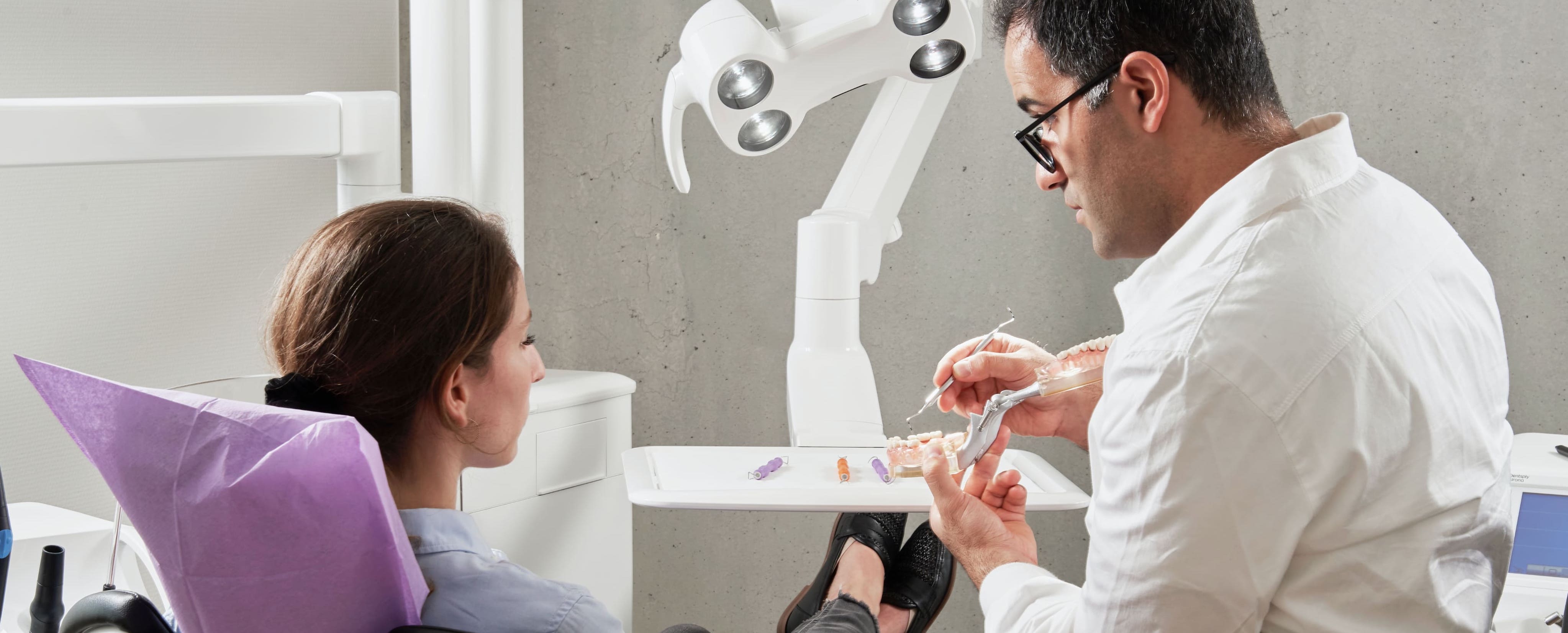 A dentist holds a human tooth in his hand in front of his patient.