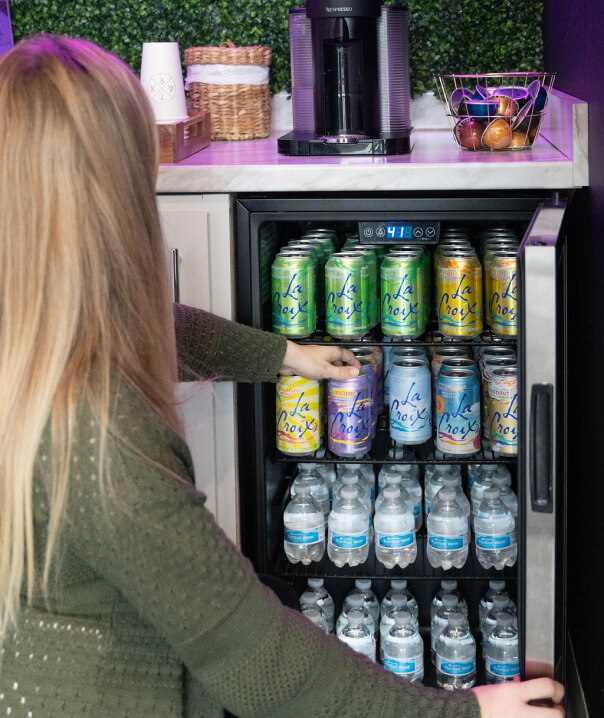 a woman reaching into a refrigerator filled with drinks