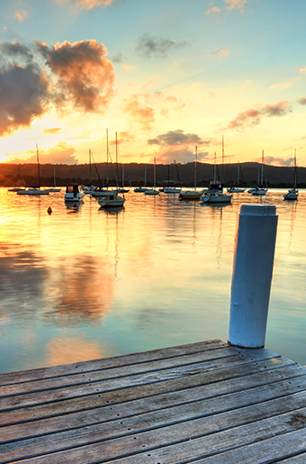 End of a pier overlooking a marina with boats at sunset.