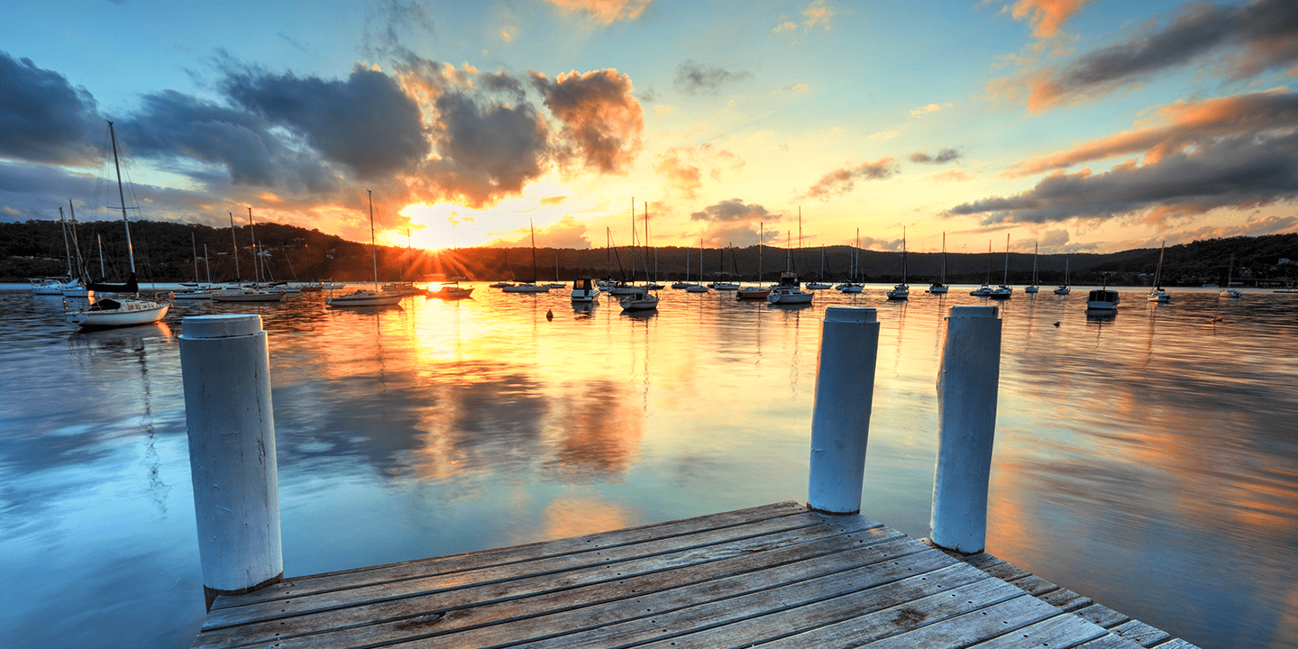 End of a pier overlooking a marina with boats at sunset.