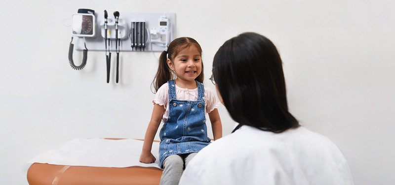 a little girl sitting on top of a table next to a doctor