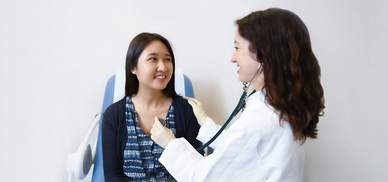 a female doctor with a stethoscope examining and talking to a female patient on a chair