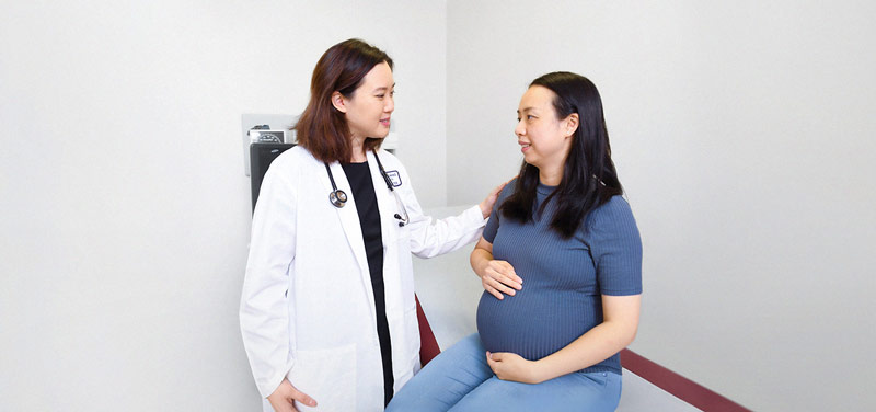 a female doctor comforting a pregnant woman seated on an examination table, with a reassuring hand on her shoulder