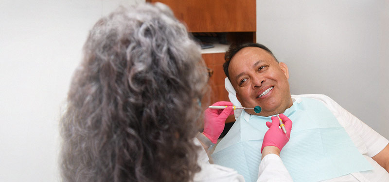 a smiling man sitting in a dentist chair having his teeth examined