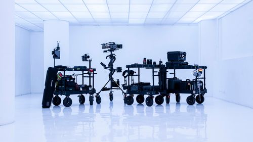camera carts loaded with video production equipment staged on a brightly-lit, reflective white set.