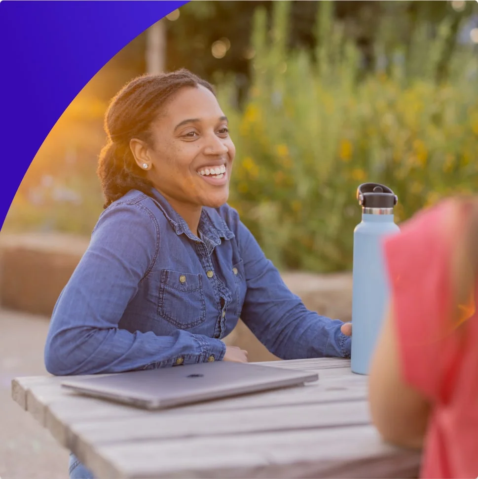 Female student with laptop and water bottle sitting outside and smiling. 