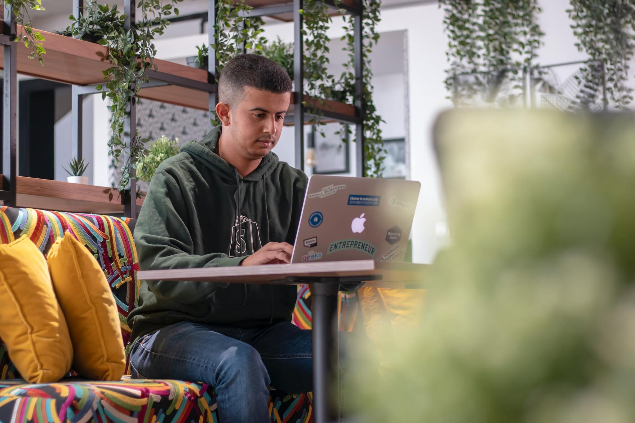 a man wearing a Shopify sweatshirt sitting on a couch with a laptop