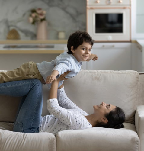 A woman with brown hair is on the couch with a child with brown hair. 