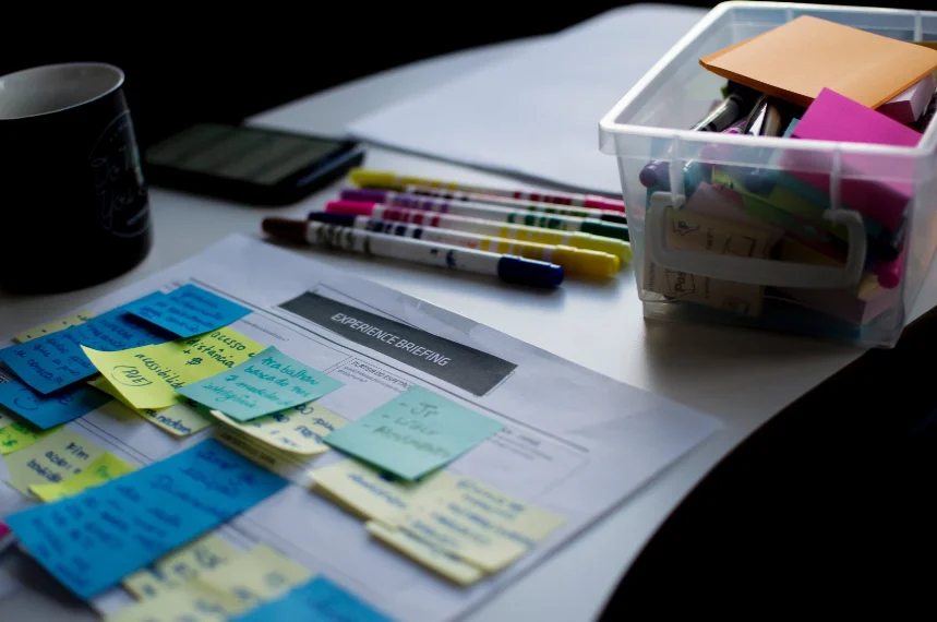 A desk with a box of colorful sticky notes and pens.