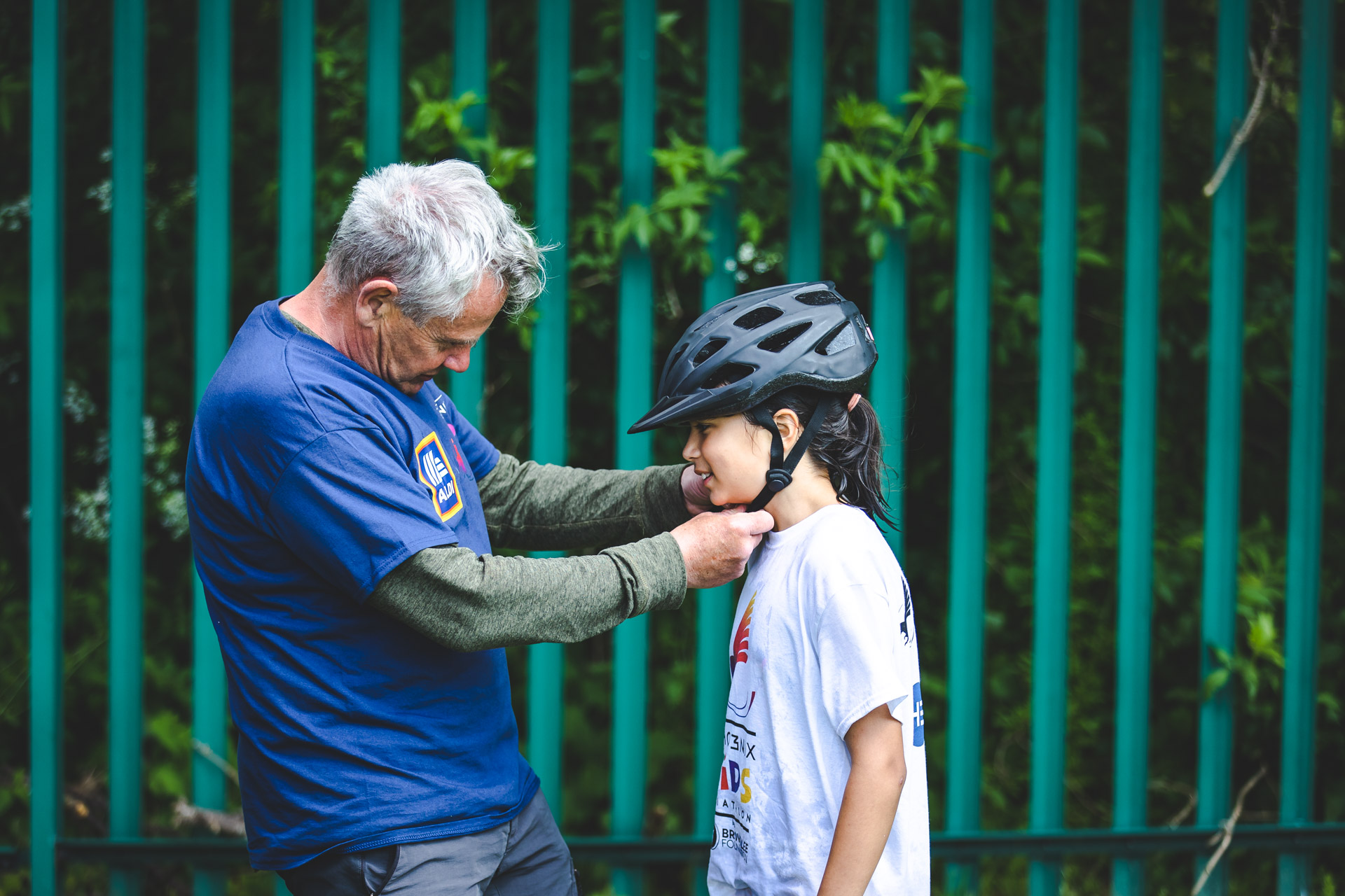 A photograph of a volunteer helping a child to fasten the helmet