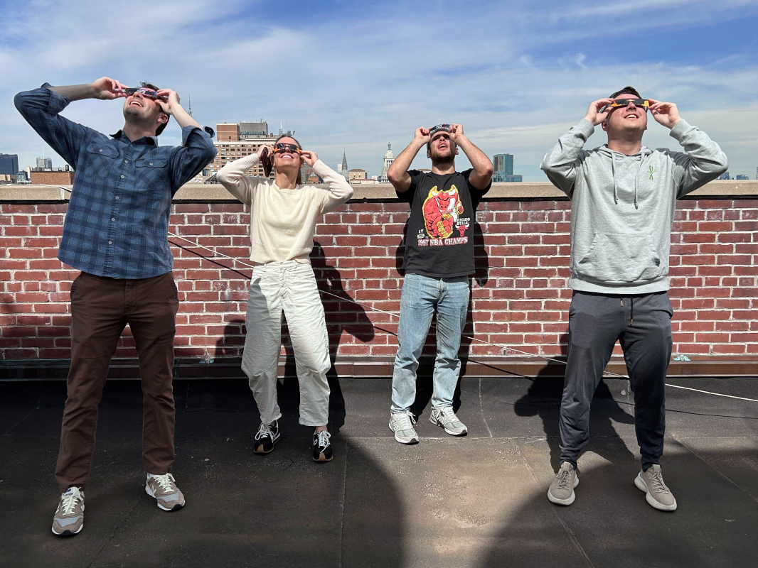 Four people look through eclipse glasses at the bright sky. 