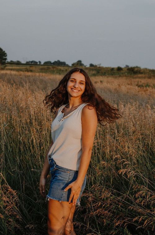 a young woman standing in front of a wheat field smiling at the camera