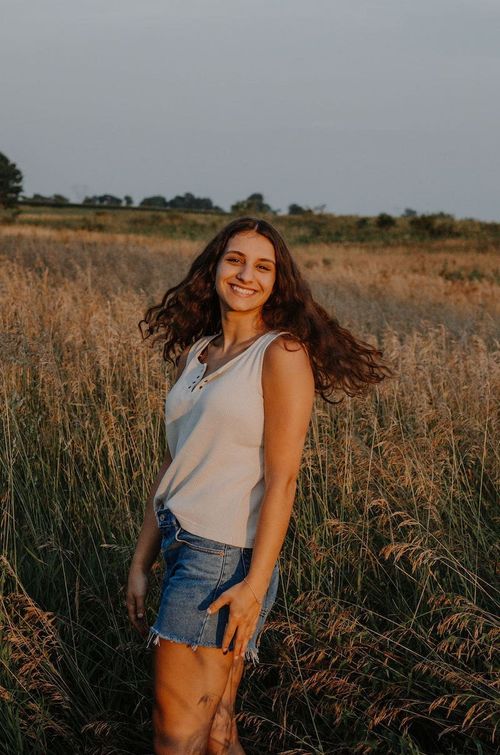 a young woman standing in front of a wheat field during sunset