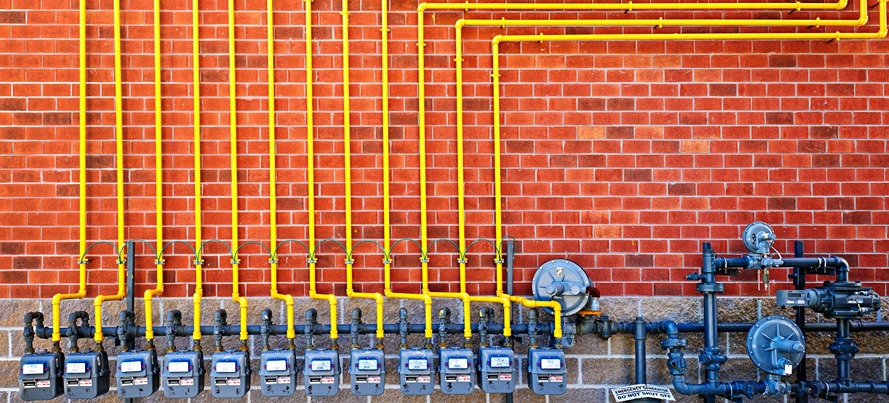 natural gas meters with yellow pipes against brick wall
